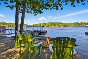 A lakeside setting with green Adirondack chairs, a campfire, and dock structures. - Lakefront Home w/ Private Dock, Boat Slip, Firepit & Sunset Views at MM5 (Gravois Mills)