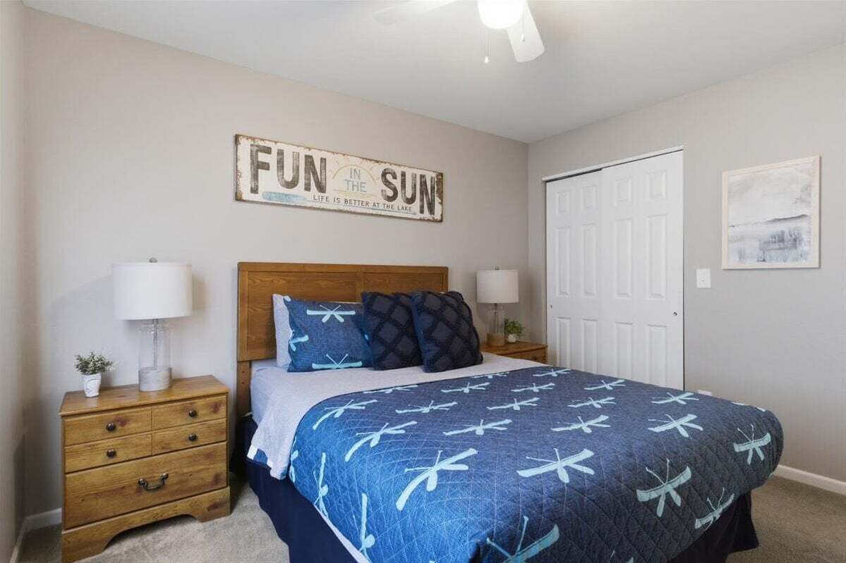 A bedroom with a bed, a nightstand, a dresser, a ceiling fan, a door, and a wall sign.