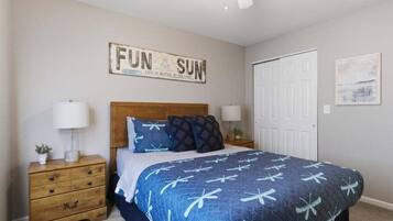 A bedroom with a bed, a nightstand, a dresser, a ceiling fan, a door, and a wall sign.