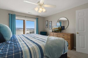 Un dormitorio con cama, cómoda, televisor y balcón con cortinas.