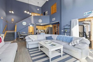 A modern living room with a large L-shaped sofa, a coffee table, and a staircase leading to an upper level. - Lakefront House w/ Private Dock, 2 Slips, Dock Bar & Kayaks at 2mm (Lake Ozark)