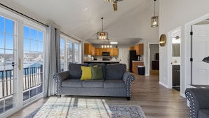A spacious living room with a gray sofa, a patterned rug, and large windows offering a view of the outside. - Runabout Retreat (Osage Beach)