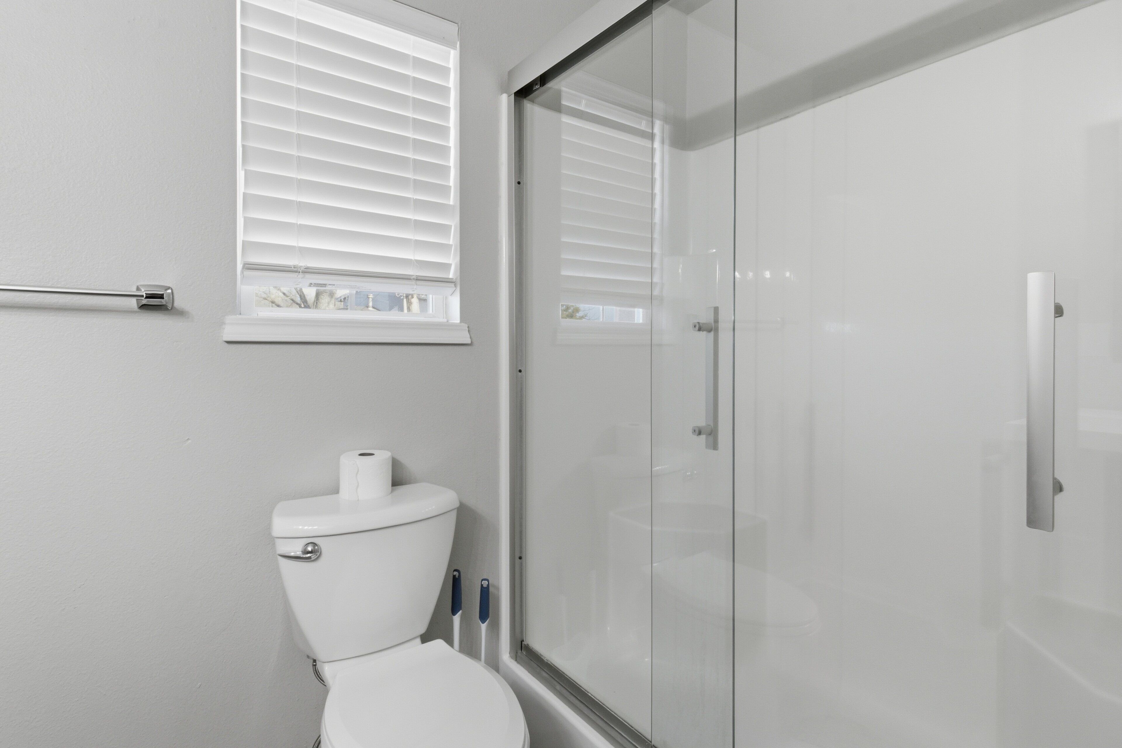A bathroom with a toilet, a glass shower enclosure, and a window with blinds.