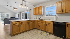 A modern kitchen with wooden cabinets, a dishwasher, and a large window. - Runabout Retreat (Osage Beach)
