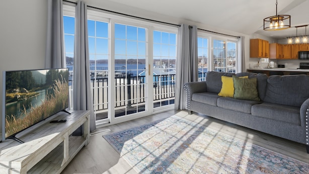 A modern living room with a large TV, a grey sofa with yellow pillows, a wooden bench, and a patterned rug. - Runabout Retreat (Osage Beach)