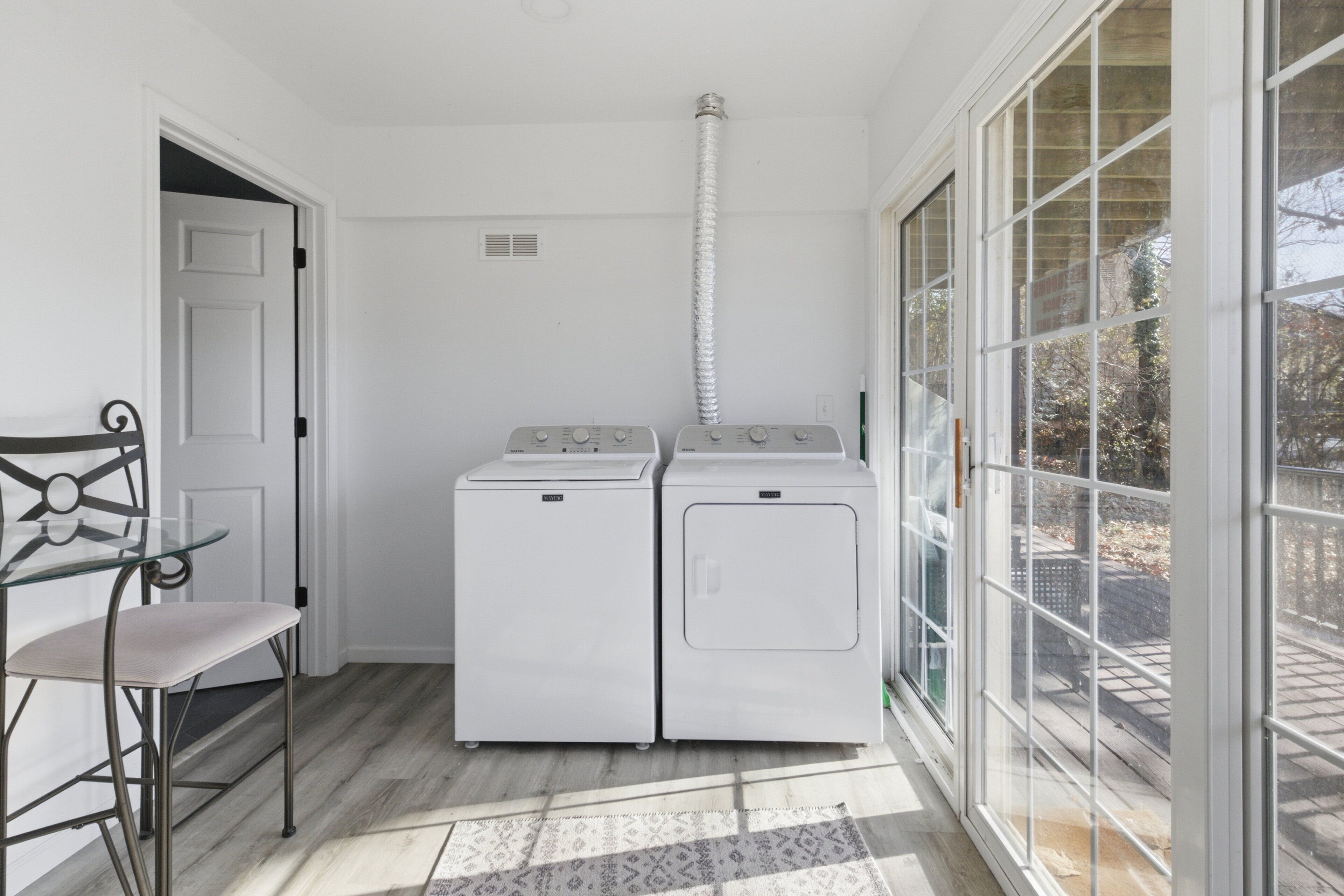 A laundry room with two white washing machines, a glass table, and a chair.