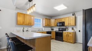 A modern kitchen with wooden cabinets, a central island with bar stools, a black stove, and a microwave. - Runabout Retreat (Osage Beach)