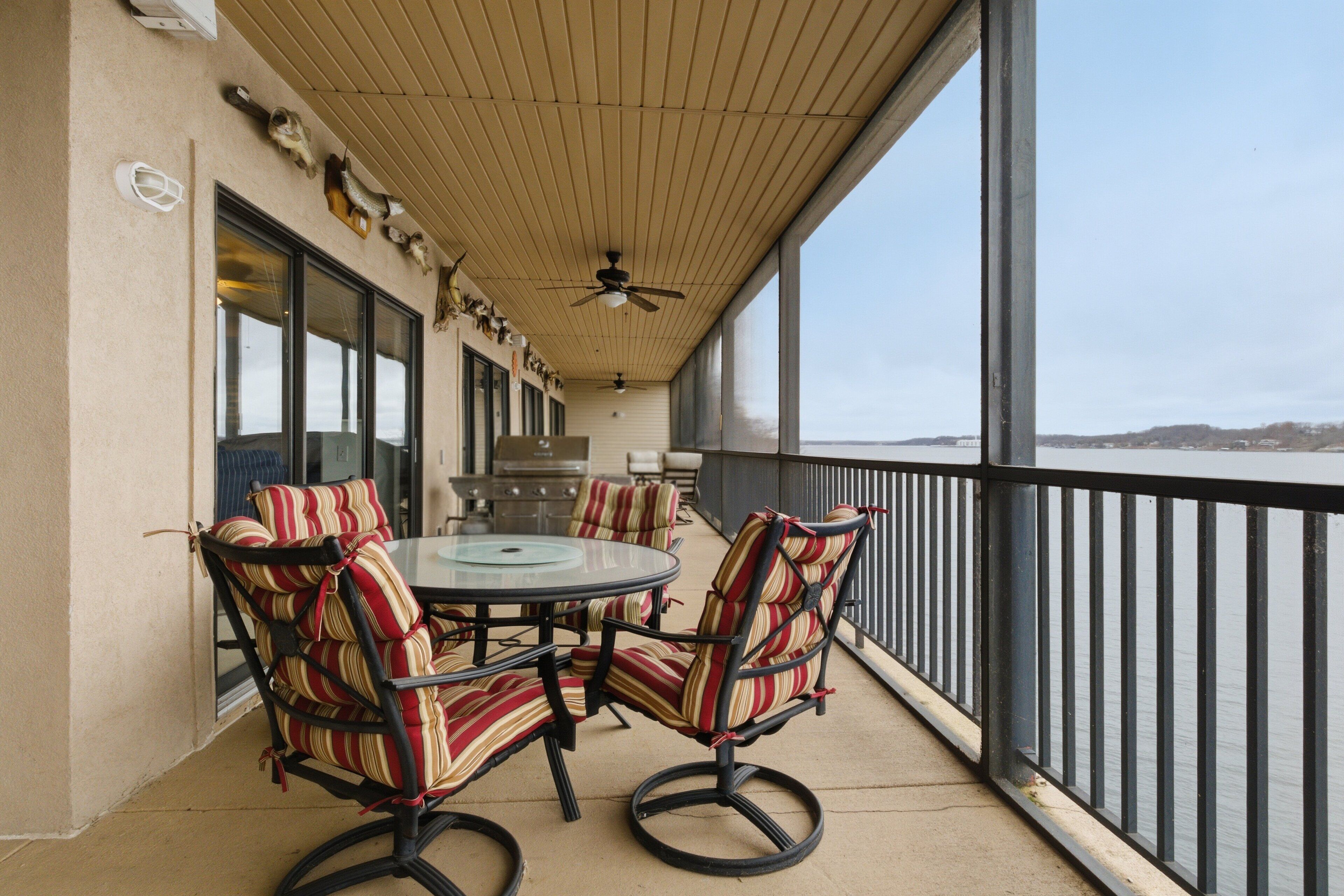 A covered outdoor seating area with a round table and striped chairs, overlooking a body of water.