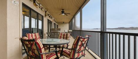 A covered outdoor seating area with a round table and striped chairs, overlooking a body of water.