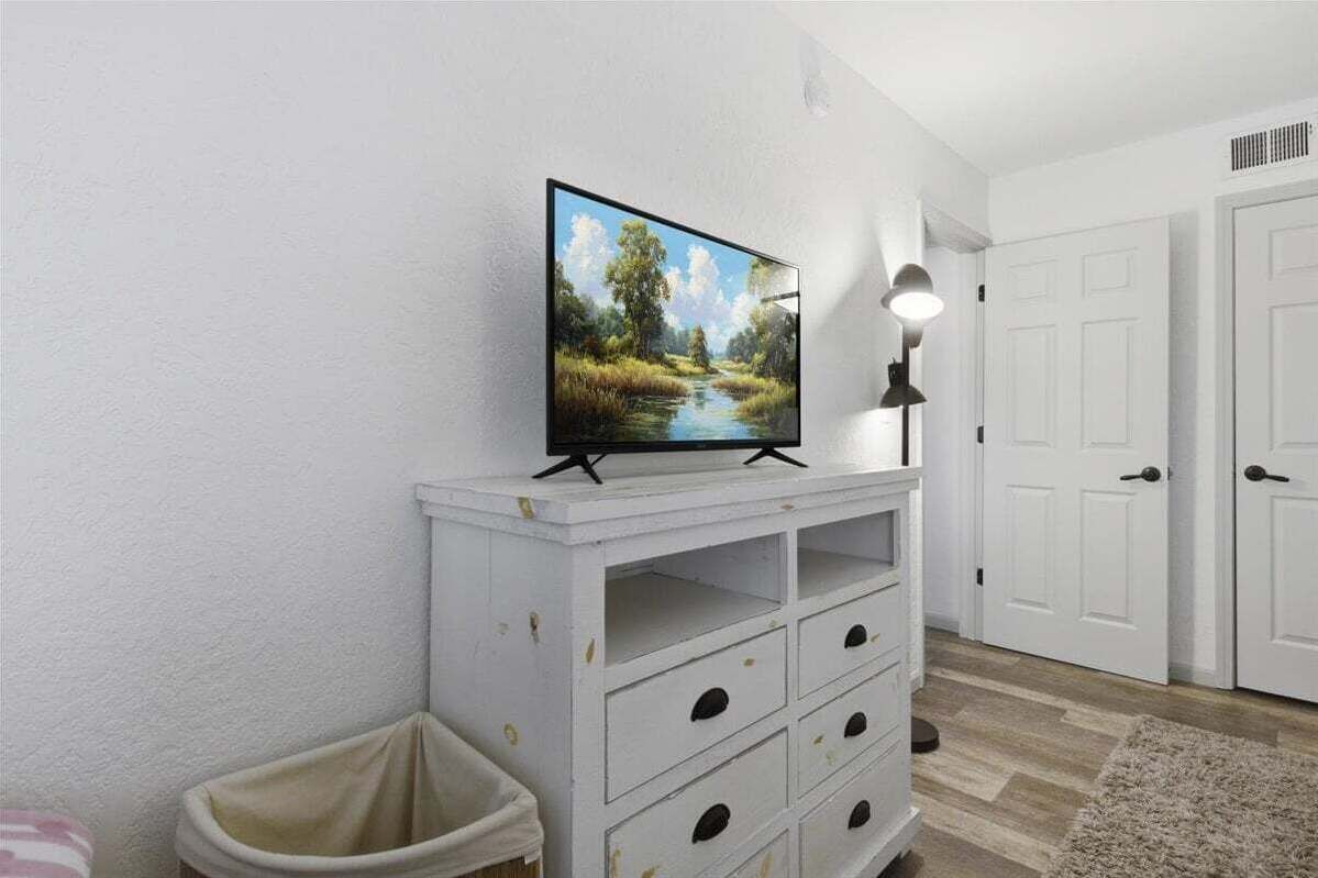Ein Zimmer mit einem weißen Schrank, einem Fernseher darauf, einer Lampe und einer Tür.