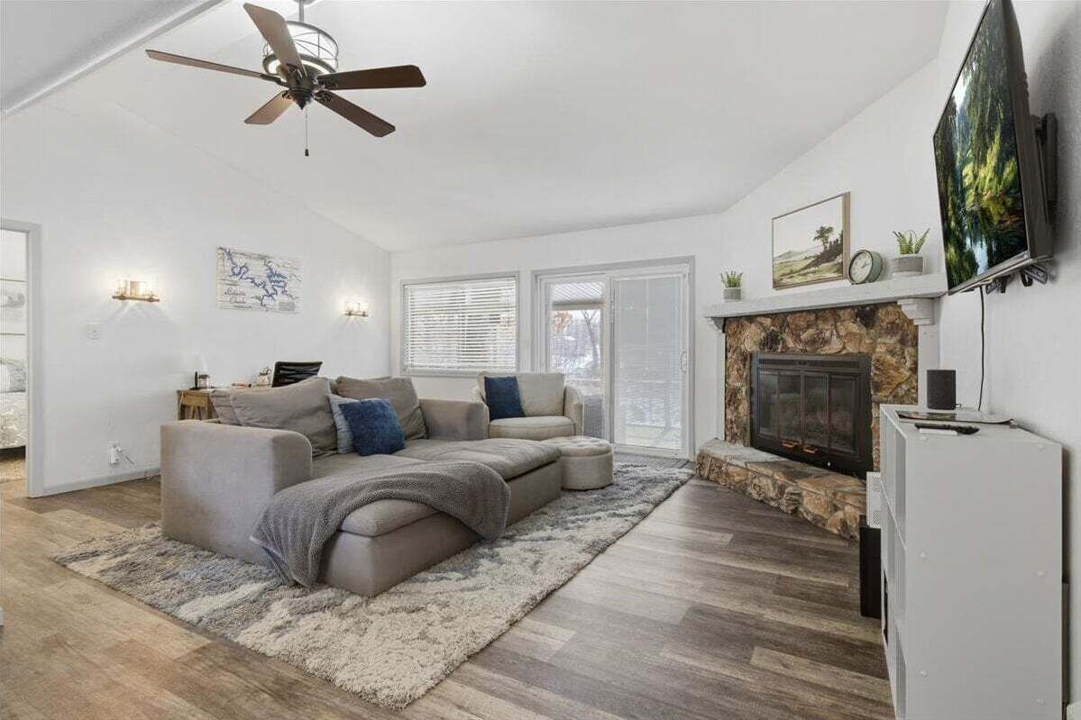 A living room with a sectional sofa, a fireplace, a ceiling fan, and a mounted TV.
