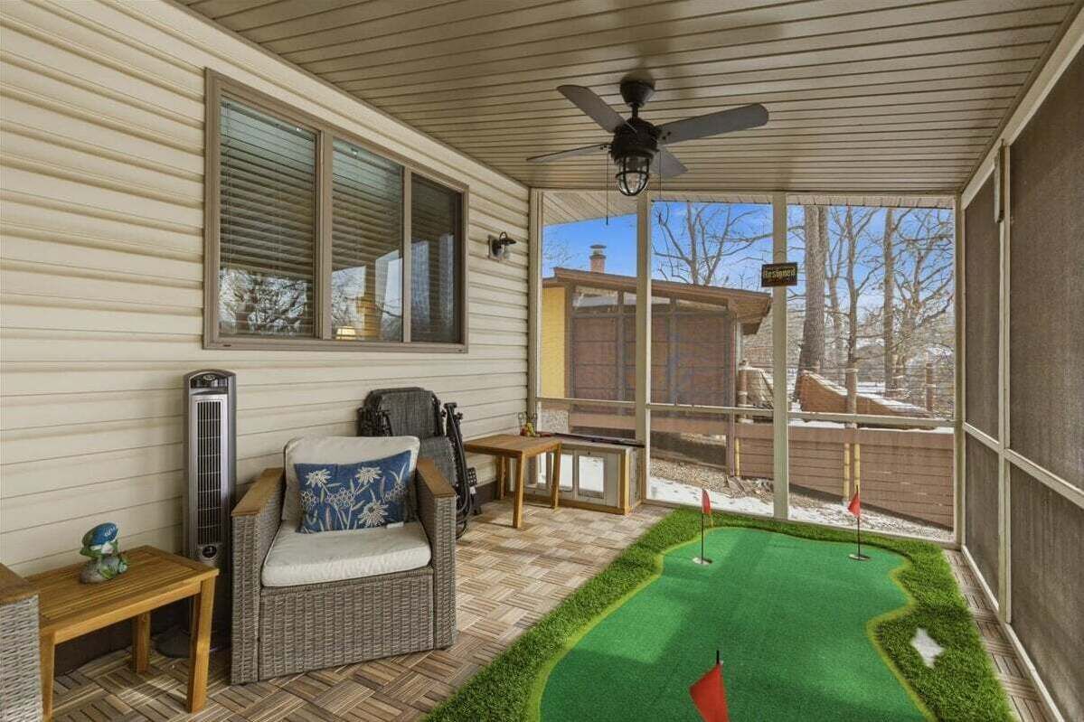 A covered patio with a small putting green, wicker furniture, and a ceiling fan.