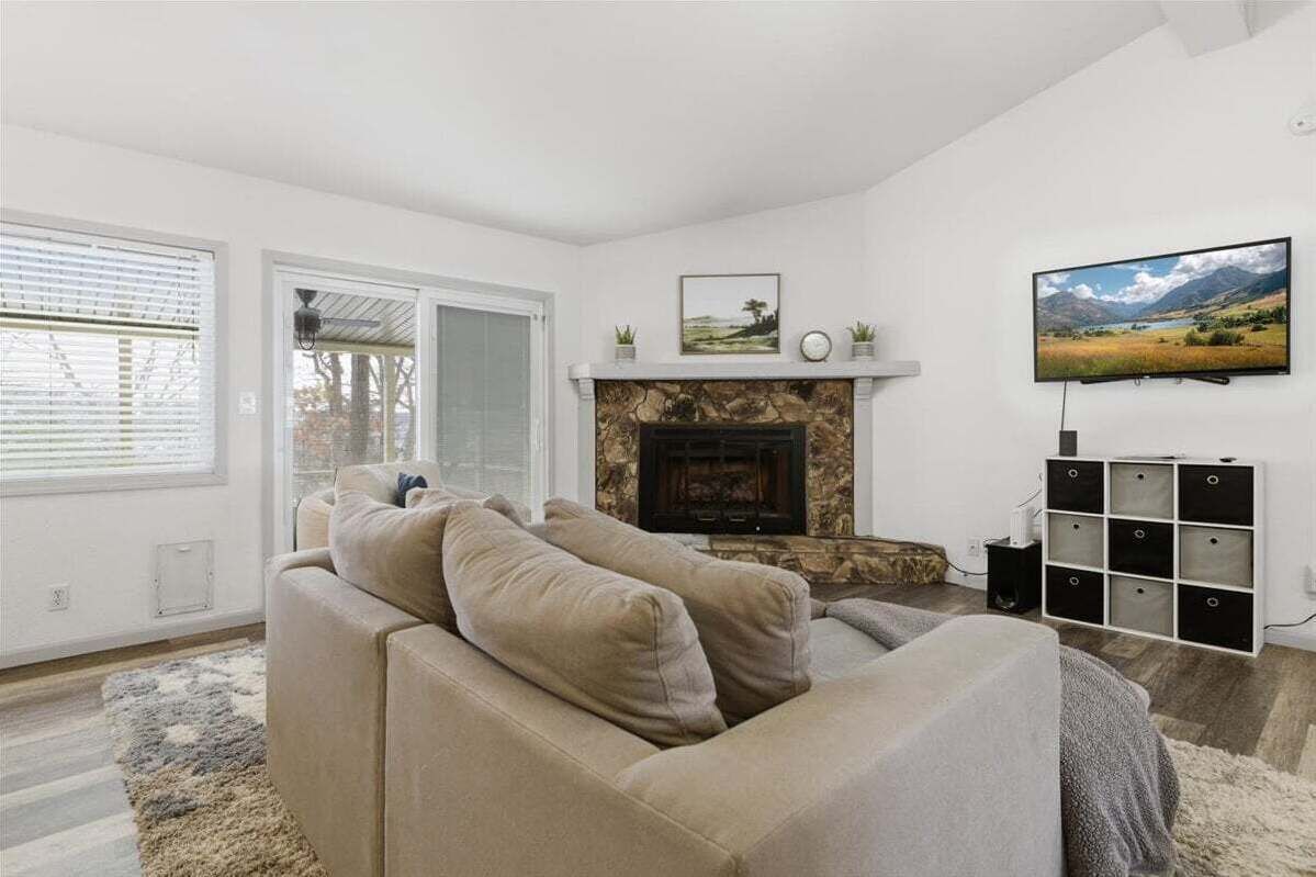 Una sala de estar con un sofá beige, una chimenea, un televisor y vistas a un paisaje a través de las ventanas.