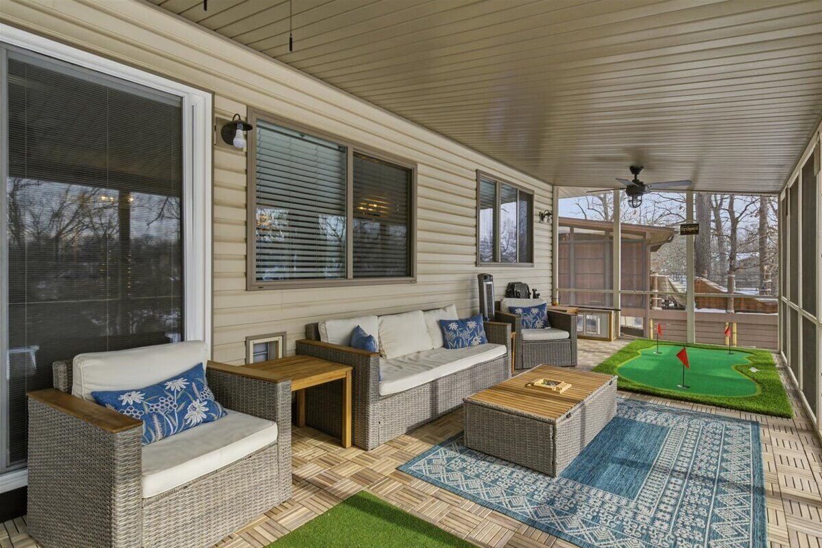 A covered patio with wicker furniture, a small table, and a green artificial turf area with flags.