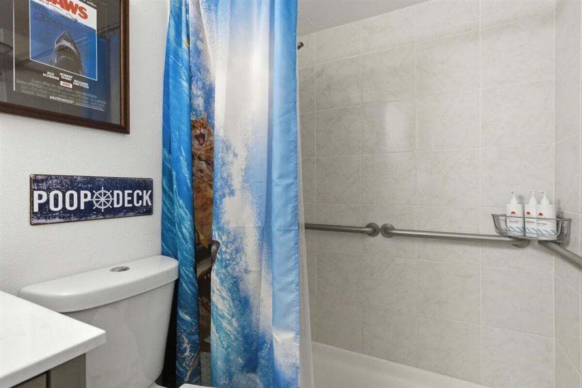Un baño con inodoro, cortina de ducha con diseño de tiburón y un letrero que dice 'POOP DECK'.