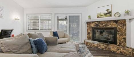 A living room with a stone fireplace, beige sofas, and a large window.