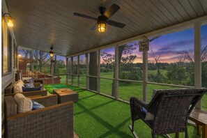 A covered outdoor seating area with wicker furniture, a ceiling fan, and a view of a sunset over a grassy landscape. - Prime Osage Beach Home, Pet-friendly w/ Garage Near Margaritaville, Dining & Golf (Osage Beach)