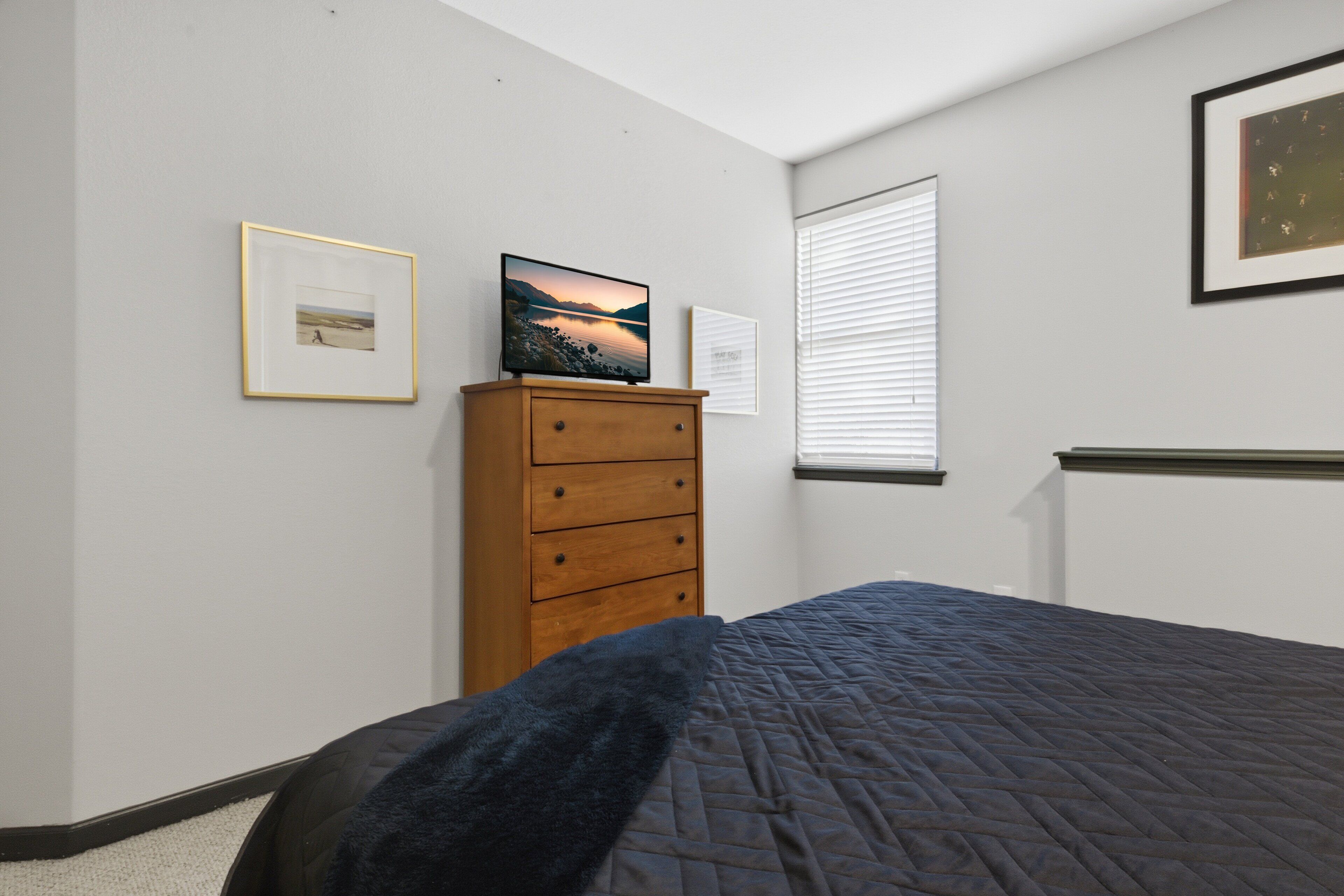 A bedroom with a bed, a dresser, and framed pictures on the wall.