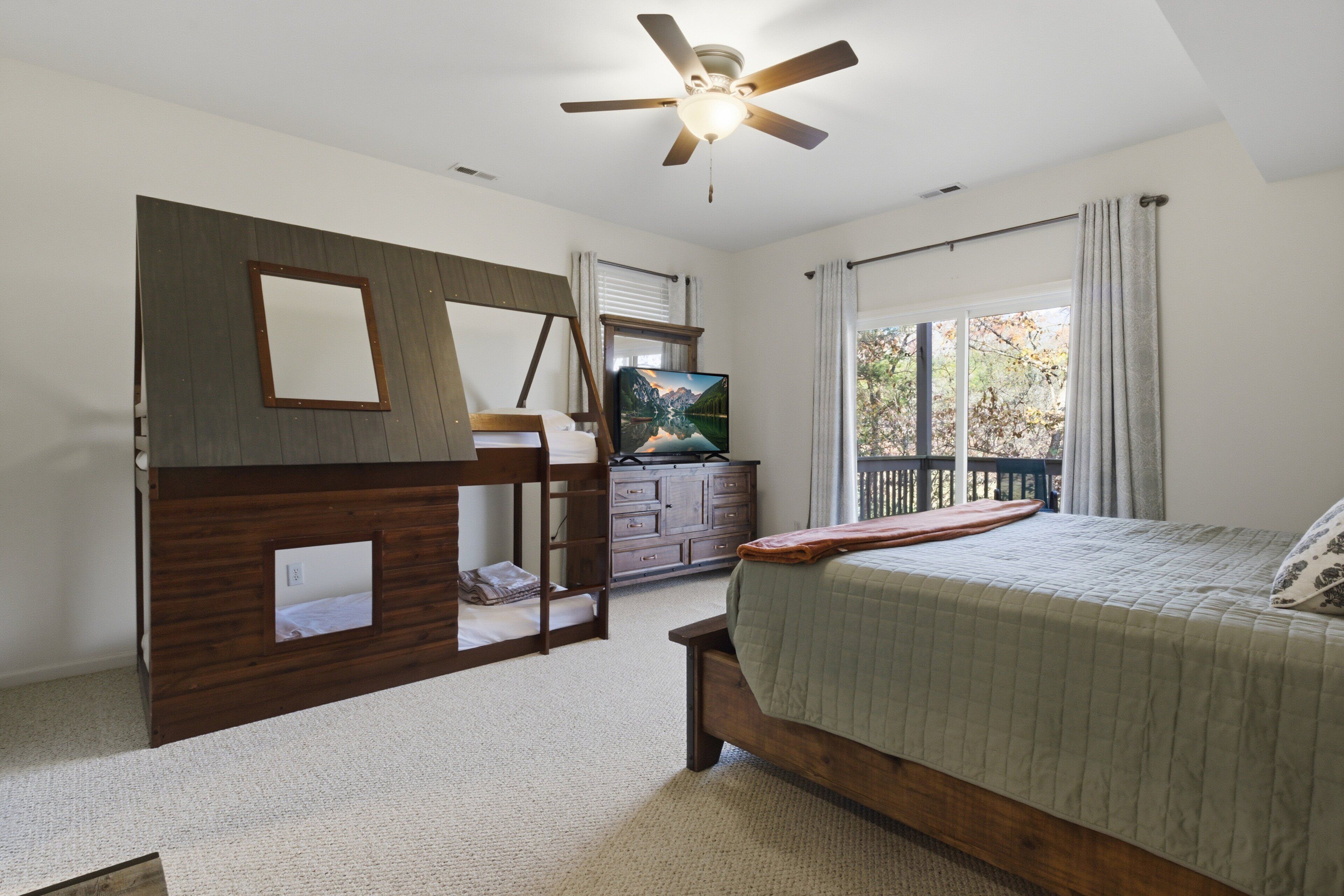 A bedroom with a bed, a dresser, a television, and a window with curtains.