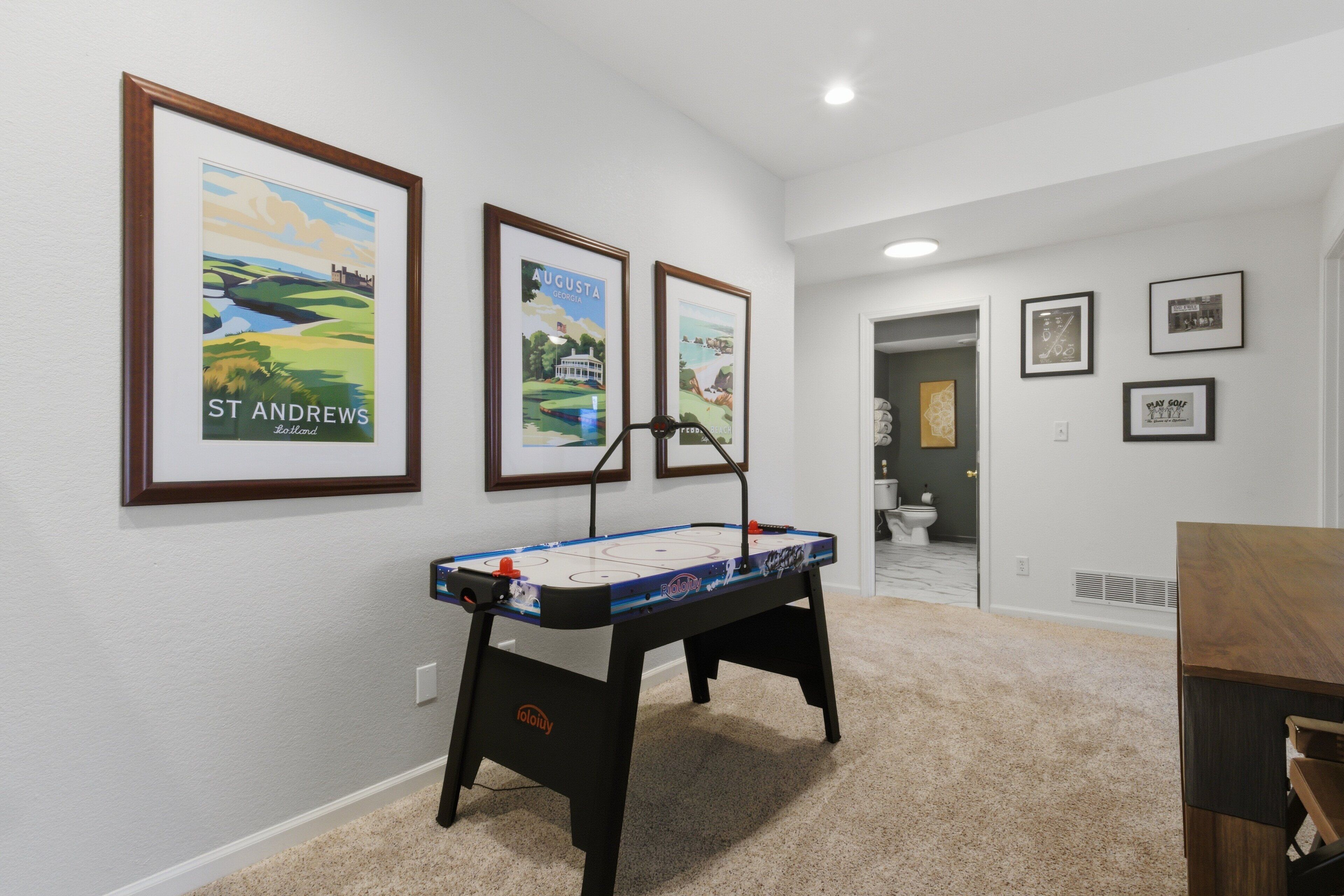 A room with a foosball table, framed posters on the wall, and a carpeted floor.