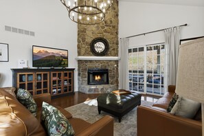 A living room with a stone fireplace, leather sofas, a television, and a view through a large window. - Old Kinderhook 2 Decks, Firepit, Kid & Pet Friendly Golf Retreat (Camdenton)