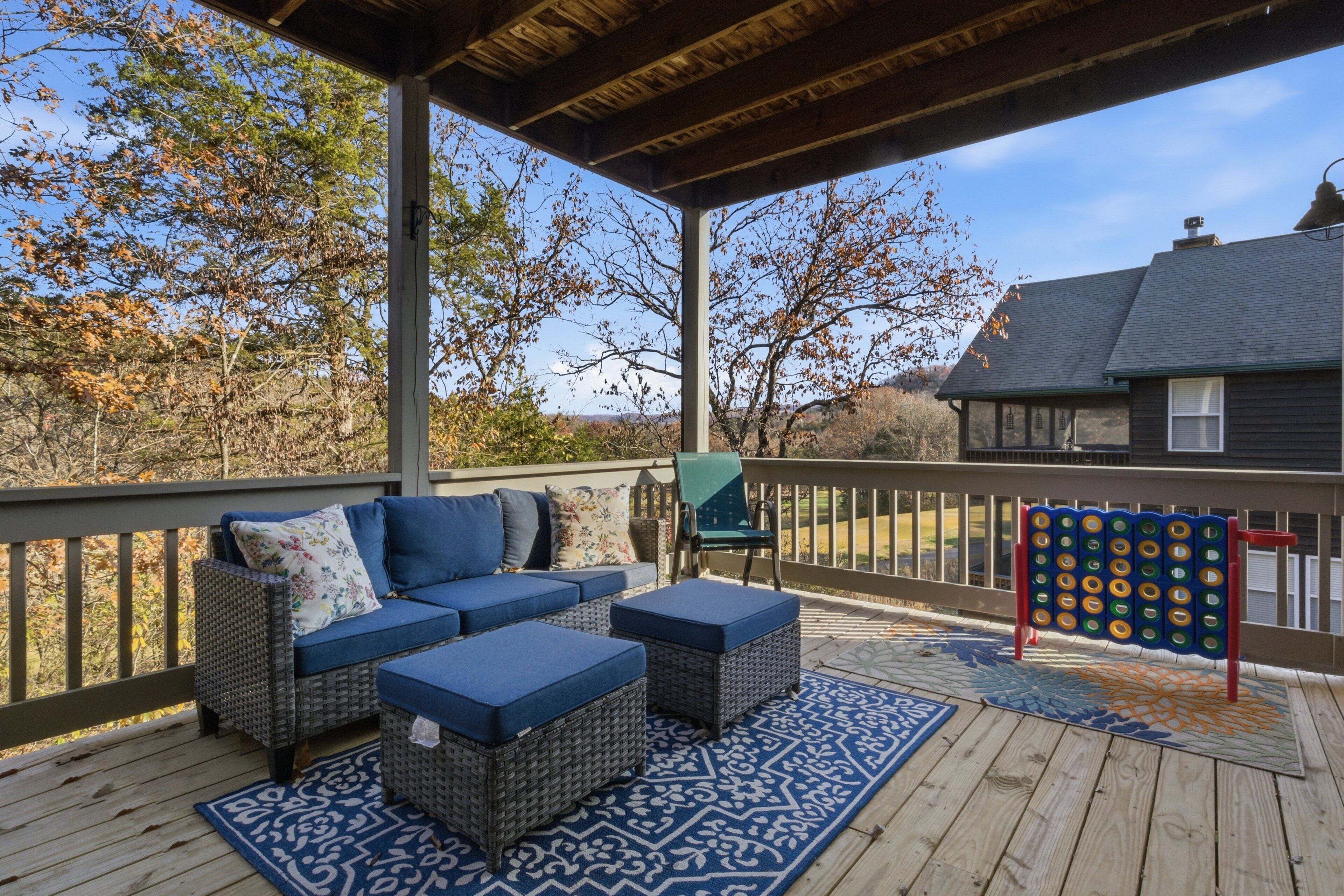 Una terraza techada con mobiliario exterior, un juego de mesa y vistas a una casa y árboles.