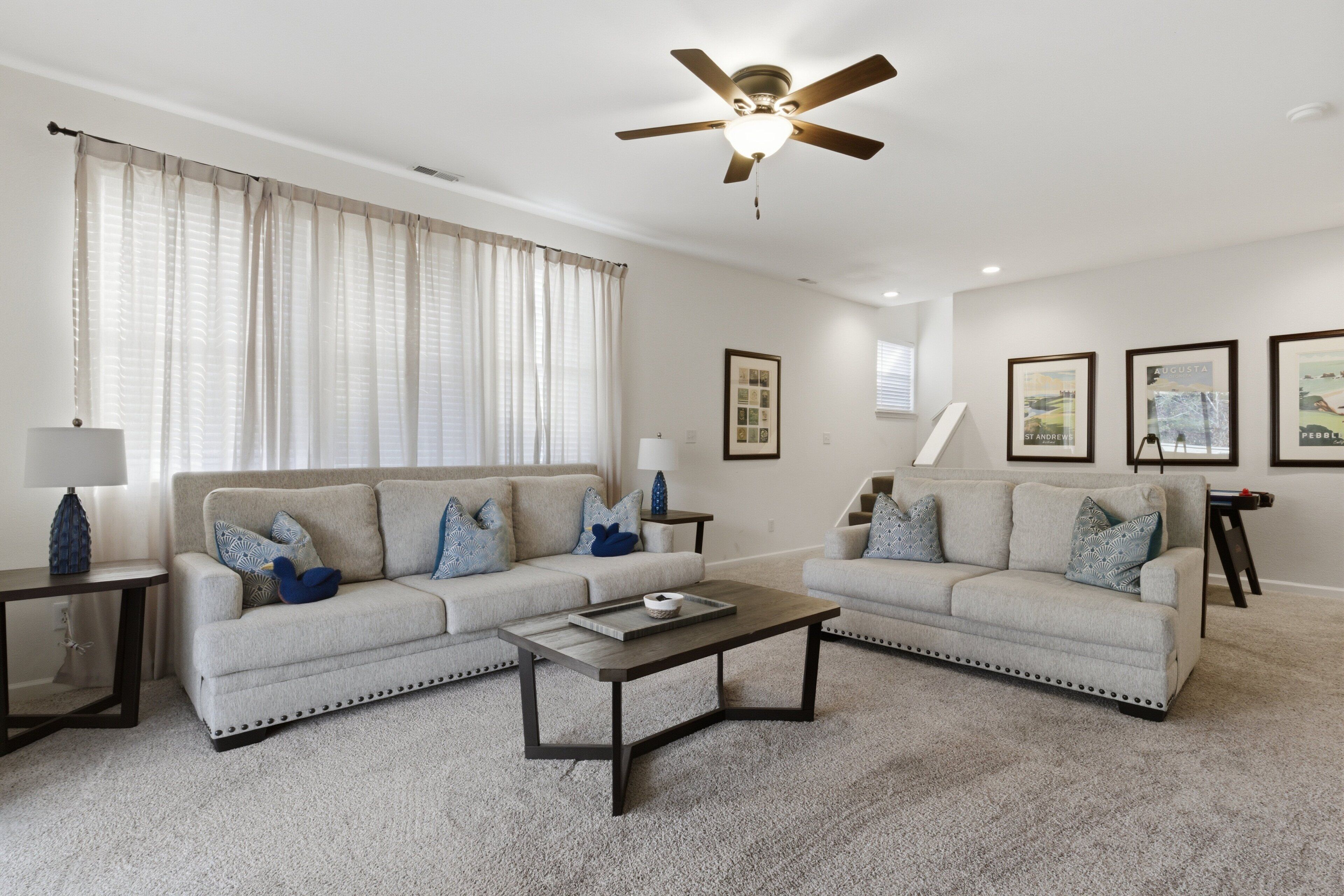 A living room with two sofas, a coffee table, a ceiling fan, and framed pictures on the wall.