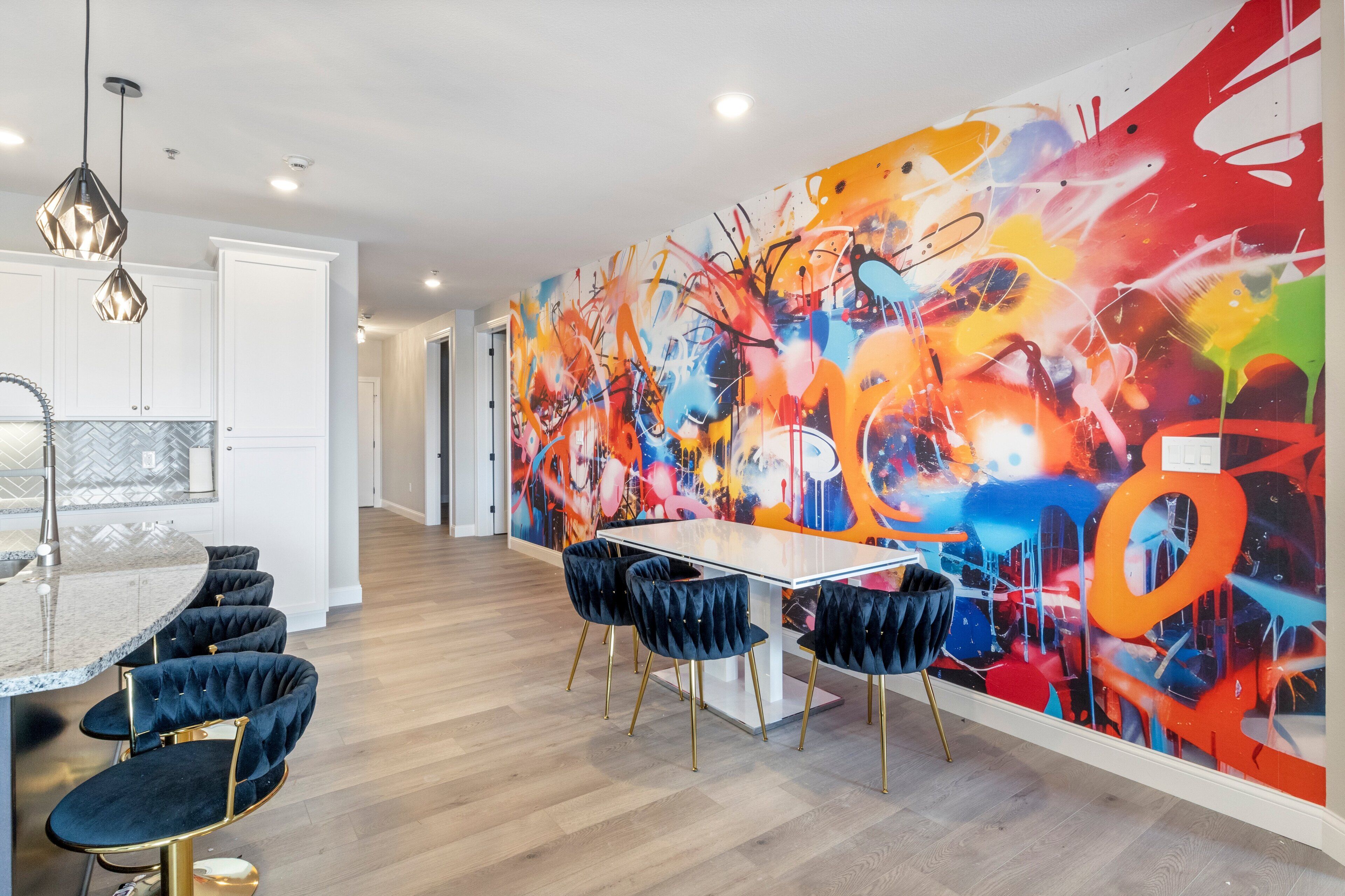 A modern kitchen with a white countertop, black bar stools, and a vibrant abstract mural on the wall.