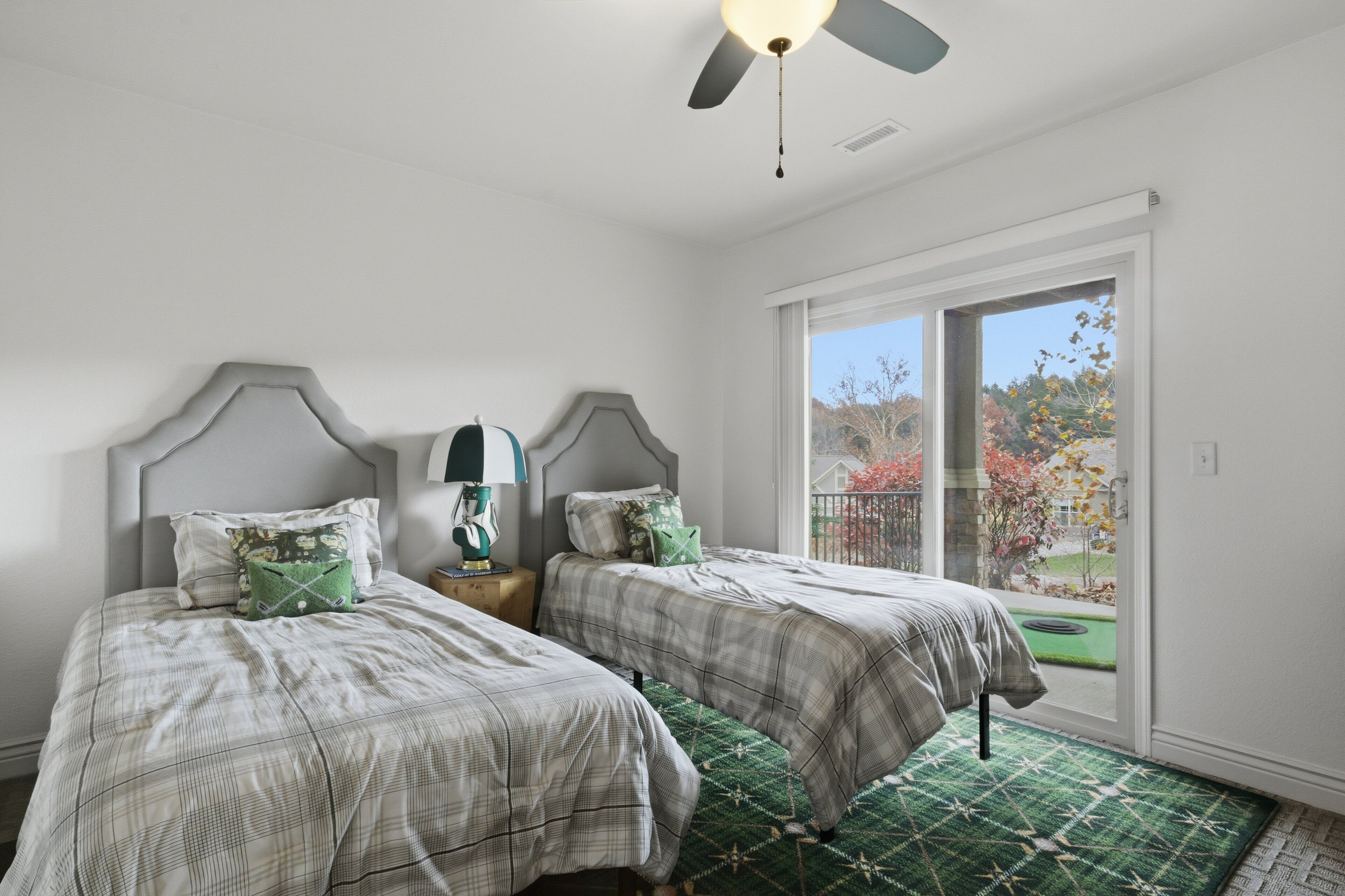 A bedroom with two beds, a ceiling fan, a window with a view of the outdoors, and a green rug.