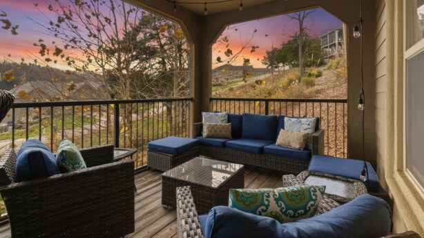 A covered outdoor seating area with wicker furniture and cushions, overlooking a scenic landscape during sunset. - Fairway Retreat (Camdenton)