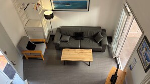 A modern living room with a grey sofa, a wooden coffee table, and a painting of a tropical scene. - Bright Duplex in Cavalière – Steps from the Beach (Le Lavandou)