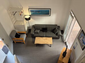 A modern living room with a grey sofa, a wooden coffee table, and a painting of a tropical scene. - Bright Duplex in Cavalière – Steps from the Beach (Le Lavandou)
