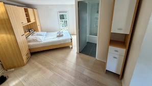 A bedroom with a wooden bed, a wardrobe, a small bathroom with a shower, and a balcony. - Bright Duplex in Cavalière – Steps from the Beach (Le Lavandou)