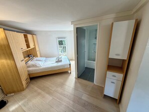 A bedroom with a wooden bed, a wardrobe, a small bathroom with a shower, and a balcony. - Bright Duplex in Cavalière – Steps from the Beach (Le Lavandou)
