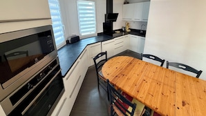 A modern kitchen with white cabinets, a wooden dining table, and a built-in oven. - Bright Duplex in Cavalière – Steps from the Beach (Le Lavandou)