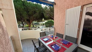 A balcony with a table set for dining, chairs, and a view of trees and a street. - Bright Duplex in Cavalière – Steps from the Beach (Le Lavandou)
