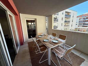Un balcón con una mesa de comedor dispuesta para seis personas, rodeado de sillas de metal blanco.