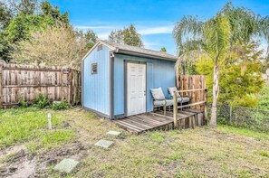 Eine kleine, blaue Gartenhütte mit Tür und einer kleinen Veranda mit einem Stuhl.
