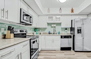 Et moderne køkken med hvide skabe, rustfrie stål-apparater og en grøn backsplash.