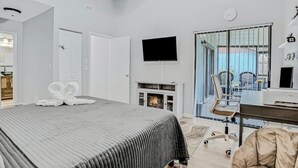 Ein modernes Hotelzimmer mit einem großen Bett, einem Flachbildfernseher, einem Kamin, einem Schreibtisch und Blick durch eine Glastür.