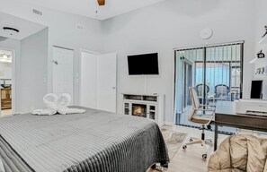 Et moderne hotelværelse med en stor seng, et fladskærms-TV, en pejs, et skrivebord og udsigt gennem en glasdør.