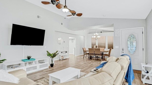 Ein geräumiges Wohnzimmer mit Flachbildfernseher, Deckenventilator, Essbereich mit Chandelier und großem Fenster mit dekorativem Spiegel.