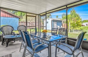 Eine überdachte Terrasse mit Glastisch und -stühlen, ein kleiner Garten und ein blauer Schuppen im Hintergrund.