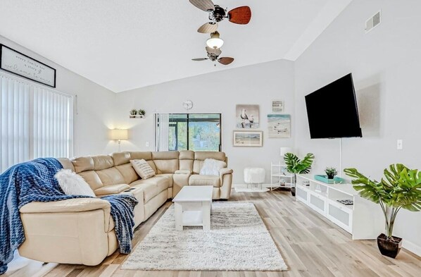 Ein modernes Wohnzimmer mit Ecksofa, Couchtisch, Fernseher und Deckenventilator.