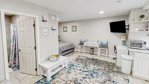 Un espacio habitable compacto con cama, escritorio pequeño, televisor y kitchenette.