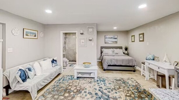Un dormitorio moderno y bien iluminado con cama, sofá, escritorio y una mesita.