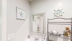 Un baño con lavamanos blanco, un espejo y repisas con toallas y artículos de aseo.