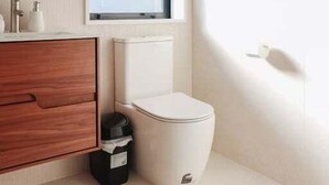 Ein modernes Badezimmer mit einem Holzbadschränkchen, einer weißen Toilette und einem Fenster mit Tageslicht.