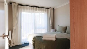 Ein Hotelzimmer mit Bett, Vorhängen, einem Fenster und einer Tür.