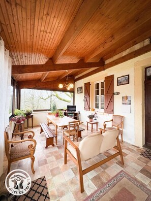 A cozy room with wooden beams, a wooden dining table, and chairs. There are potted plants and a television on a table. - Gîtes de France® - Patou's Gîte (CATUS)